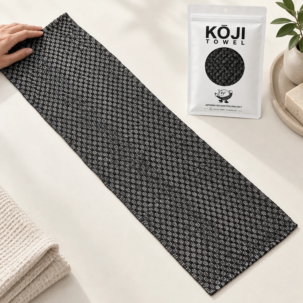 Rozłożony Kōji Towel obok dłoni i opakowania